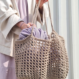 May include: A beige crocheted tote bag with a wide, open weave. The bag is filled with a skein of lavender yarn.