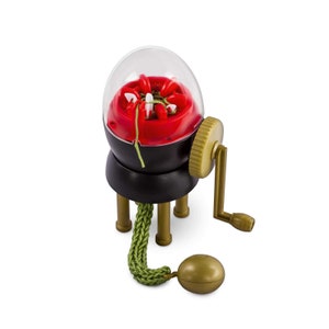 Könnte beinhalten: Ein roter und schwarzer Plastik-Strickrahmen mit einer durchsichtigen Plastikkuppel. Der Strickrahmen hat einen Kurbelgriff und sechs Stricknadeln. Grünes Garn ist durch den Strickrahmen gefädelt und eine gestrickte Schnur hängt unten heraus.