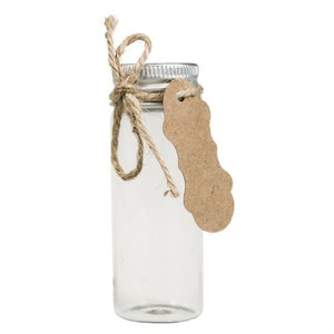 Op de afbeelding: Een heldere glazen fles met een zilveren deksel en een bruin papieren label vastgebonden met touw. De fles is leeg en klaar om te worden gevuld.