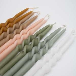 Puede incluir: Un conjunto de velas retorcidas en varios colores, incluyendo blanco, verde, melocotón, marrón y beige. Las velas están todas retorcidas y tienen un aspecto rústico y hecho a mano.