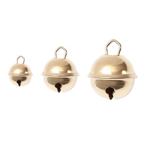Può includere: Tre campanelle dorate di diverse dimensioni appese su uno sfondo bianco.