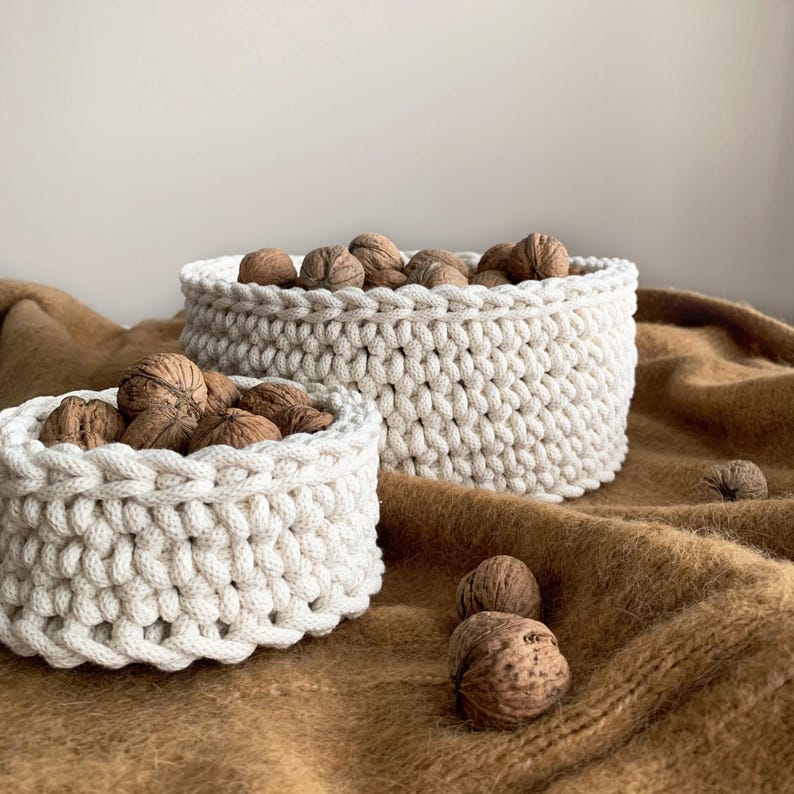 May include: Two white crocheted baskets filled with walnuts on a brown fuzzy surface. The smaller basket is in front of the larger basket.