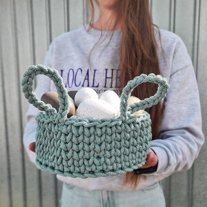 May include: A green crocheted basket with two handles filled with white and brown speckled Easter eggs.