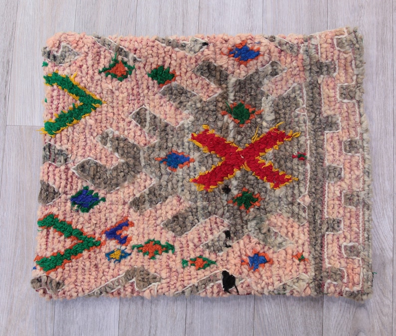 Pu&ograve; includere: Un tappeto marocchino rosa e grigio con un motivo geometrico e accenti colorati. Il tappeto ha un bordo a frange ed &egrave; fatto di lana.