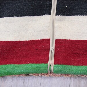 Pu&ograve; includere: Un cuscino a righe colorate con una chiusura a zip. Il cuscino &egrave; realizzato in tessuto tessuto con strisce nere, bianche, rosse e verdi.