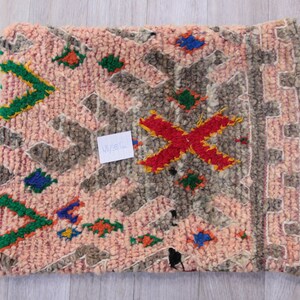 Pu&ograve; includere: Un tappeto marocchino rosa e grigio con un motivo geometrico in tonalit&agrave; di verde, rosso, blu e giallo. Il tappeto ha un bordo a frangia e misura 45x38 cm.