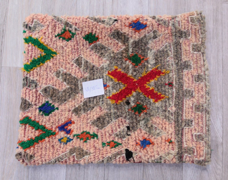 Pu&ograve; includere: Un tappeto marocchino rosa e grigio con un motivo geometrico in tonalit&agrave; di verde, rosso, blu e giallo. Il tappeto ha un bordo a frangia e misura 45x38 cm.