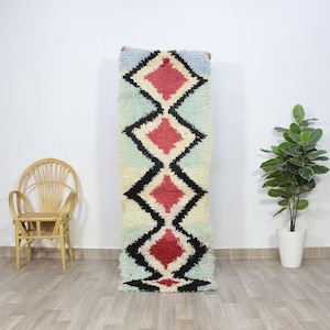 May include: A long, rectangular rug with a geometric pattern in shades of blue, white, black, and red. The rug has a fluffy, textured surface.