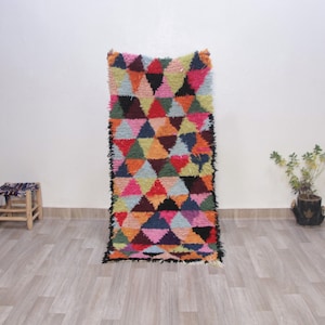 May include: A colorful Moroccan rug with a geometric pattern of triangles in shades of pink, blue, green, yellow, orange, and red. The rug has a black fringe border.
