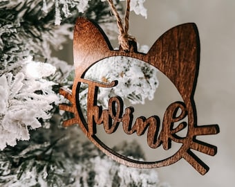 Könnte beinhalten: Ein hölzerner Weihnachtsbaumschmuck in Katzenform mit dem Wort "Twink" ausgeschnitten in der Mitte.