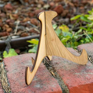 May include: A wooden display stand with a natural wood finish. The stand has a triangular shape with three legs and a curved top.