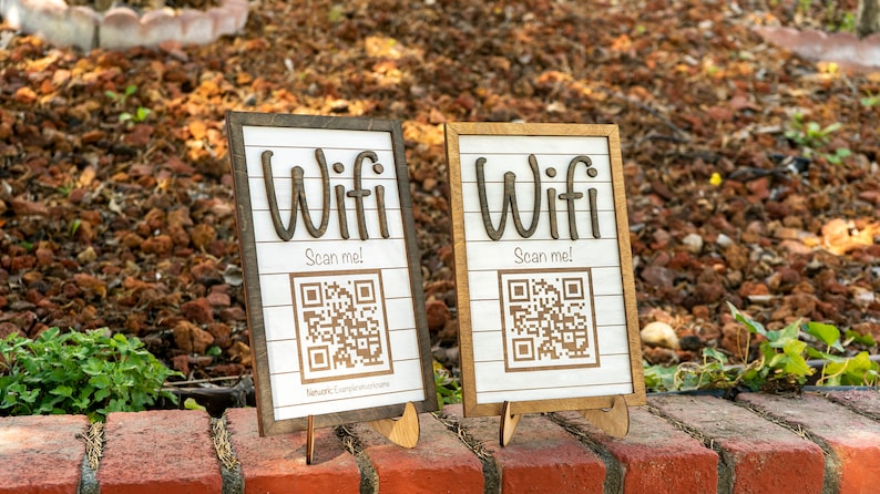 May include: Two wooden signs with a white background and brown wood frames. Each sign says "Wifi Scan me!" and has a QR code. The signs are on small wooden stands.