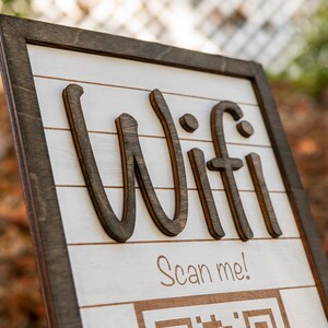 May include: A wooden sign with the word "Wifi" written in large, stylized letters. The sign also includes the text "Scan me!" and a QR code.