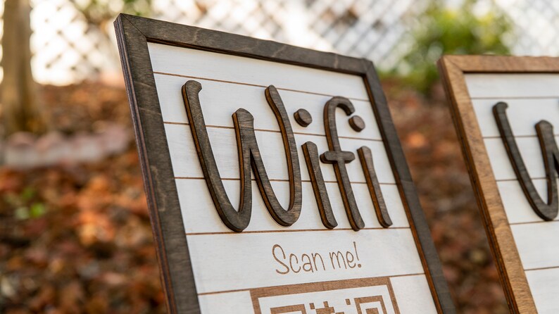 May include: A wooden sign with the word "Wifi" written in large, stylized letters. The sign also includes the text "Scan me!" and a QR code.