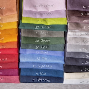 May include: A stack of 49 fabric swatches in various colours, including red, blue, green, yellow, and brown. Each swatch has a number and a name printed on it, such as "1. Black", "2. Slate", "3. Grey", "4. Light grey", "5. Cacao", "6. Fog", "7. Limed oak", "8. Oat", "9. Blue", "10. Old navy", "11. Light blue", "12. Bluet", "13. Sky", "14. Basil", "15. Green", "16. Sage", "17. Hunter", "18. Lime", "19. Lavender", "20. Pink Opal", "21. Sandstone", "22. Honey", "23. Canary", "24. Dijon", "25. Mustard", "26. Terracotta", "27. Red", "28. Classic red", "29. Wine", "30. Plum", "31. Salmon", "32. Striped 1", "33. Natural beige", "34. White", "35. Milk", "36. Black", "37. Slate", "38. Grey", "39. Light grey", "40. Cacao", "41. Fog", "42. Limed oak", "43. Oat", "44. Blue", "45. Old navy", "46. Light blue", "47. Bluet", "48. Sky", "49. Basil".