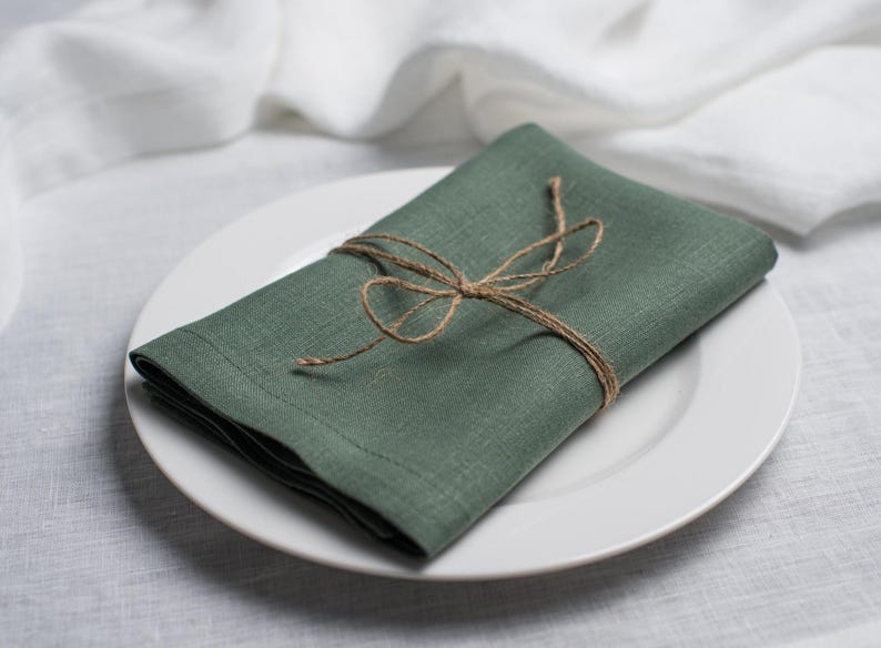 Basil green linen napkin folded and tied with rustic natural twine, beautifully styled on a white ceramic plate. Elegant organic linen table textile designed for sustainable dining, modern table decor, intimate dinners, wedding receptions, farmhouse interiors and seasonal entertaining. Soft washed linen with a rich natural texture, reusable eco friendly cloth napkin for everyday meals, cottagecore styling, luxury tablescapes, holiday gatherings and timeless handmade home decor.