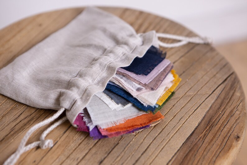 May include: A linen drawstring bag filled with a stack of colorful fabric scraps. The fabric scraps are in various shades of blue, purple, orange, yellow, and brown.