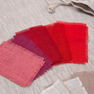 May include: A set of six fabric swatches in various shades of red, from a deep burgundy to a bright scarlet. The swatches are arranged in a fan shape and have a rough, textured surface.