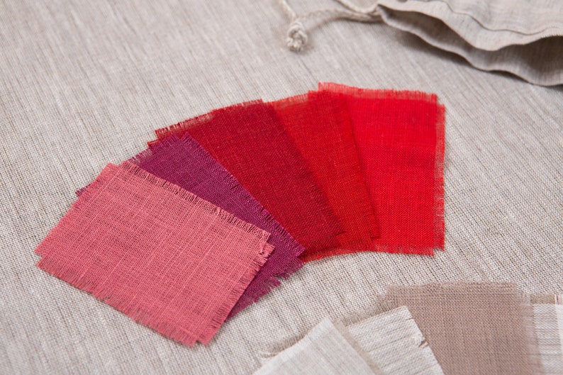 May include: A set of six fabric swatches in various shades of red, from a deep burgundy to a bright scarlet. The swatches are arranged in a fan shape and have a rough, textured surface.