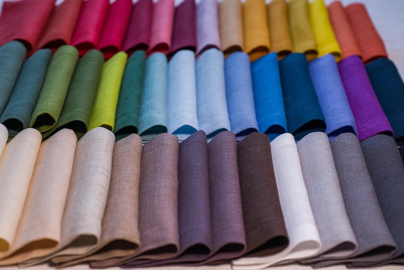 May include: A collection of folded linen napkins in a spectrum of colors, including red, pink, green, blue, and purple. The napkins are arranged in rows, showcasing a variety of hues and textures. The image highlights the diverse color palette.