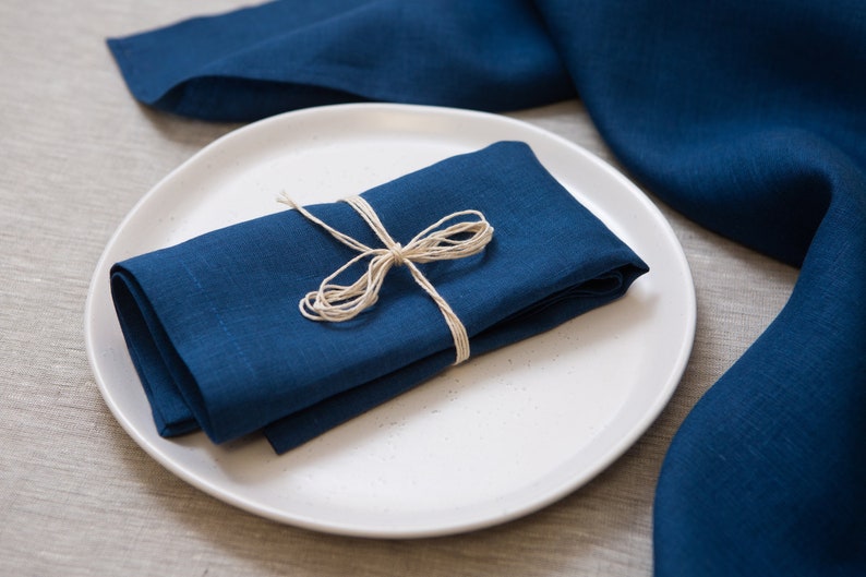 Deep blue linen napkin folded and tied with rustic natural twine, beautifully styled on a white ceramic plate. Elegant organic linen table textile designed for sustainable dining, modern table decor, intimate dinners, wedding receptions, farmhouse interiors and seasonal entertaining. Soft washed linen with a rich natural texture, reusable eco friendly cloth napkin for everyday meals, cottagecore styling, luxury tablescapes, holiday gatherings and timeless handmade home decor.