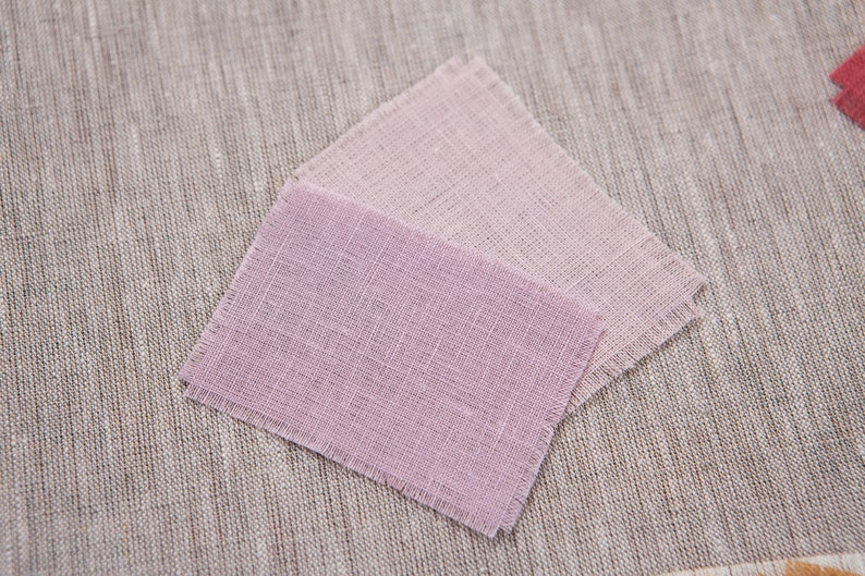 May include: Two squares of fabric in shades of pink, with a slightly darker pink on top. The fabric has a textured, woven appearance.