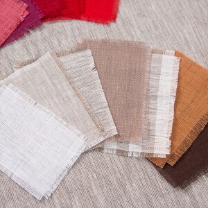 May include: A collection of fabric swatches in various colors and textures, including white, beige, brown, orange, and red. The swatches are arranged in a fan shape on a textured beige surface.