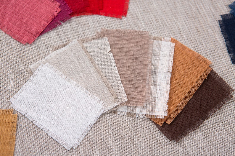 May include: A collection of fabric swatches in various colors and textures, including white, beige, brown, orange, and red. The swatches are arranged in a fan shape on a textured beige surface.