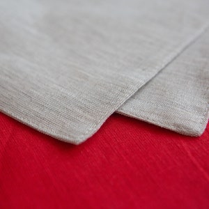 May include: A close-up of two folded linen napkins. The top napkin is a light beige color, and the bottom napkin is a vibrant red. The fabric has a textured appearance, suggesting a natural fiber like linen or cotton. The napkins are likely for dining.