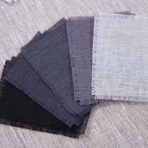 May include: A set of fabric swatches in various shades of gray, from black to light gray, with a single white swatch. The swatches are arranged in a fan shape and have a frayed edge.