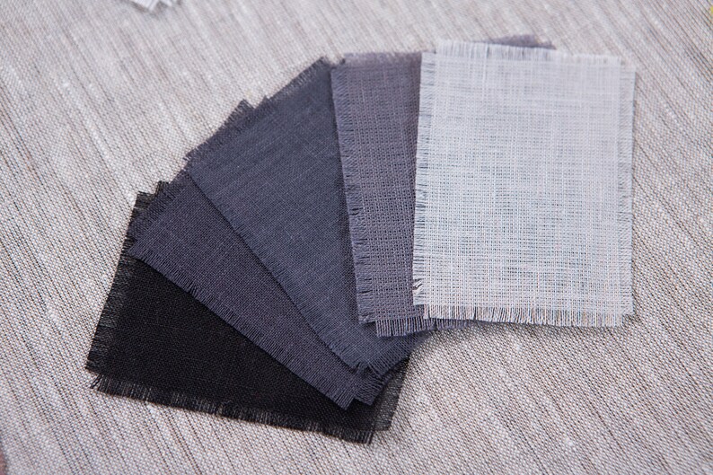 May include: A set of fabric swatches in various shades of gray, from black to light gray, with a single white swatch. The swatches are arranged in a fan shape and have a frayed edge.