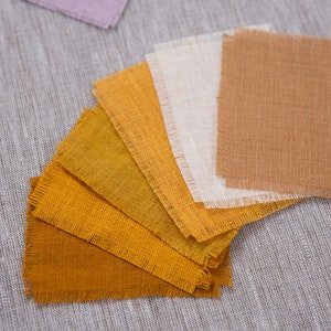 May include: A set of fabric swatches in various shades of yellow and brown, arranged in a fan shape. The swatches are made of a natural linen fabric with a slightly rough texture.