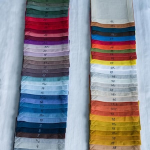 May include: Two stacks of folded fabric swatches in various colors, including green, red, blue, and yellow. Each swatch has a number written on it. The swatches are likely for textiles or home decor.