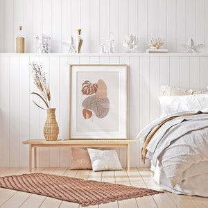 May include: A framed print with a minimalist abstract design featuring brown and beige leaves and shapes on a light pink background. The print is hanging on a white wall above a wooden bench with a brown and beige rug in front of it.