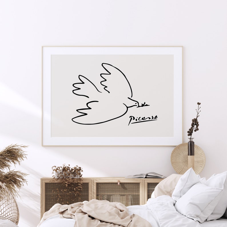 May include: A black and white line drawing of a dove with its wings spread, holding a branch in its beak. The drawing is signed "Picasso" in the bottom right corner. The drawing is framed and hanging on a white wall.