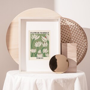 Puede incluir: Una impresi&oacute;n enmarcada con fondo blanco y una ilustraci&oacute;n de flores verdes y blancas. El texto "FLOWER MARKET TOKYO" est&aacute; impreso en negro en la parte inferior de la ilustraci&oacute;n.