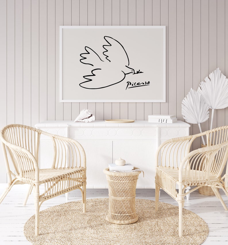 May include: A black and white line drawing of a dove in flight with the signature "Picasso" below. The artwork is framed and hanging on a white wall above a white dresser with two wicker chairs and a wicker side table.