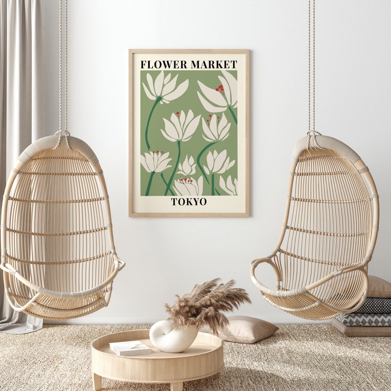 Puede incluir: Una impresi&oacute;n floral verde y blanca con el texto "FLOWER MARKET TOKYO" en un marco de madera. La impresi&oacute;n est&aacute; colgada en una pared blanca entre dos sillas de mimbre colgantes.