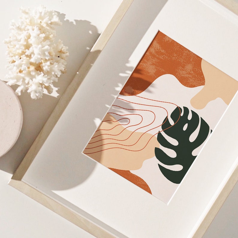 May include: A framed print with an abstract design featuring a large green leaf, orange and peach colored shapes, and thin red lines. The print is set against a white background.