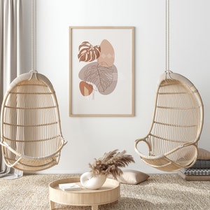 May include: Two hanging wicker chairs with a minimalist line art print of leaves and abstract shapes in shades of brown and pink. The print is framed and hanging on a white wall.