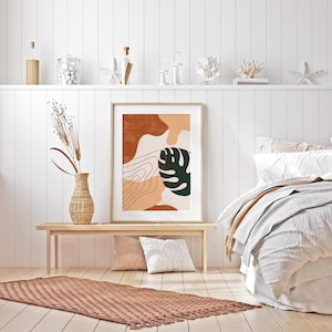 May include: A framed abstract print with a brown, orange, and green color scheme. The print features a stylized leaf and organic shapes. The print is hanging on a white wall above a wooden bench and a brown rug.