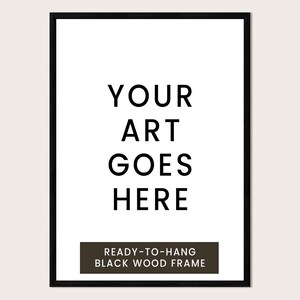 a black and white text-based design with the phrase "YOUR ART GOES HERE" prominently displayed. Below the main text, there is a smaller text that reads "READY-TO-HANG BLACK WOOD FRAME".