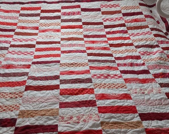 Puede incluir: Una colcha roja y blanca con un patrón a cuadros. La colcha está hecha de diferentes telas y tiene un diseño acolchado.