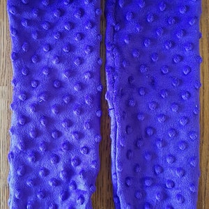 Puede incluir: Un par de calcetines de color morado y peludos con un patrón de puntos texturizados. Los calcetines están hechos de una tela suave y afelpada.