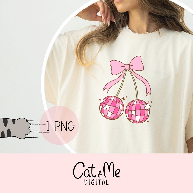 Pode incluir: Uma camiseta branca com um la&ccedil;o rosa e duas cerejas rosas em forma de bola de discoteca. As cerejas t&ecirc;m um contorno branco e est&atilde;o penduradas no la&ccedil;o. O texto "Cat & Me Digital" est&aacute; na parte inferior da imagem.