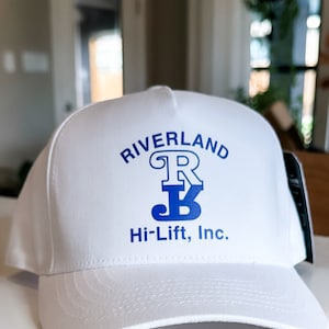 May include: White baseball cap with a blue logo that says "Riverland R Hi-Lift, Inc."