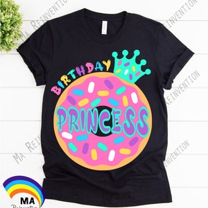 May include: Black t-shirt with a donut graphic and the text "Birthday Princess" in colorful letters. A crown with sprinkles is on top of the donut.