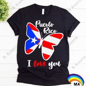 May include: Black t-shirt featuring a white butterfly design. The butterfly's wings are patterned with the colours of the Puerto Rican flag: red, white, and blue. The text "Puerto Rico" is above the butterfly and "I love you" is below it.