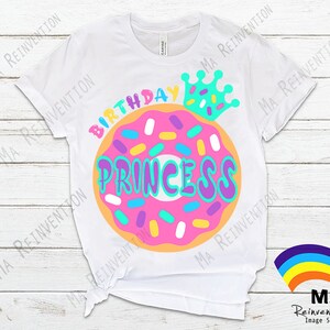 May include: White t-shirt with a pink and orange donut with sprinkles and the text "Birthday Princess" in colorful letters. A blue crown with white stars is above the donut.