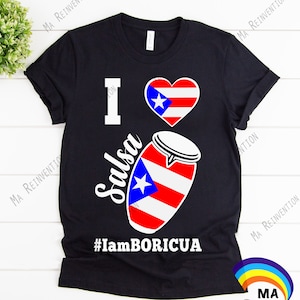 May include: Black t-shirt with a white heart featuring the Puerto Rican flag, the word "Salsa" written vertically, and the text "#IamBORICUA".